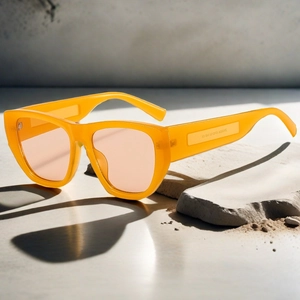 Detail of yellow acetate sunglasses with orange lenses resting on a natural stone base