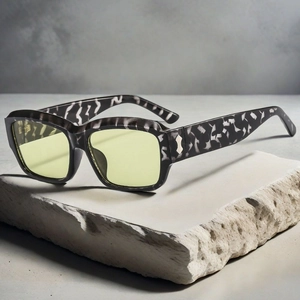 Détail de lunettes de soleil carrées effet marbre avec verres jaunes sur socle en pierre