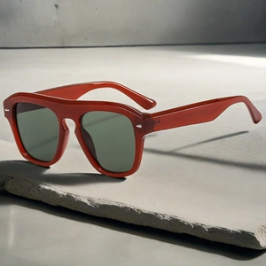 Detail of red oversized square frame sunglasses with green lenses on a grey stone surface