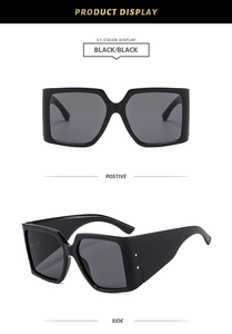 Détail de lunettes de soleil carrées noires avec rivets dorés sur les branches larges et épaisses