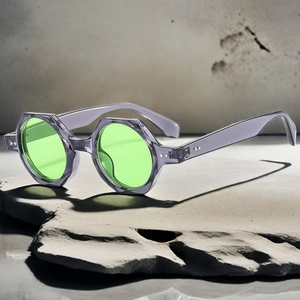 Octagonal grey resin frame sunglasses with green lenses on a concrete base