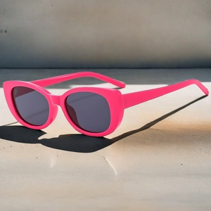 Detail view of pink cat-eye sunglasses with dark grey lenses in natural sunlight