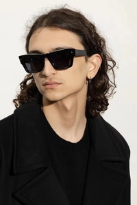 Close-up of black rectangular sunglasses worn with a black coat on a model