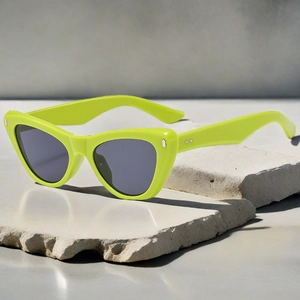 Detail of neon cat-eye sunglasses with silver metal rivets on a stone textured surface