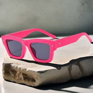 Detail of bright pink square sunglasses with metal rivets on textured stone background