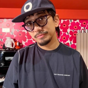 Modern oval black frame sunglasses worn by a stylish man against a floral wallpaper background