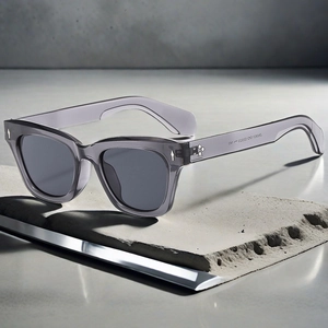 Detail of square smoke grey sunglasses featuring silver arrow rivets on concrete block