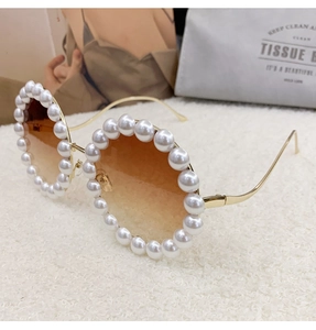 Detailed view of luxury round sunglasses with white pearl trim and golden metal temples