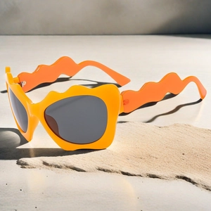 Detail showing orange irregular wavy frame sunglasses with grey lenses on a stone display