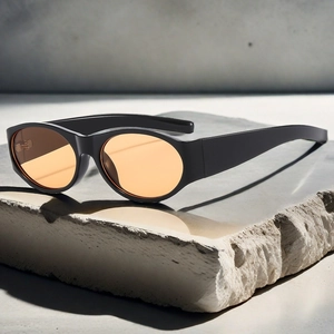 Retro oval sunglasses with black frames and orange lenses on a grey stone texture