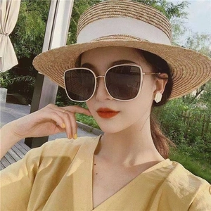 Detail of square oversized sunglasses with gold metal temples worn with a straw hat