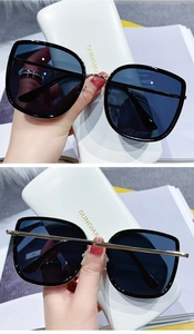 Detail of oversized black and gold sunglasses with white leather case and metal temples