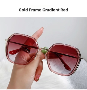 Detail of square gold frame sunglasses with red gradient lenses on a plush white background