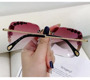 Detail einer randlosen lila Sonnenbrille mit Blumenverzierung und goldenen Metallbügeln