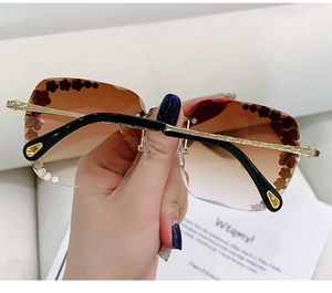 Details einer randlosen braunen Verlaufs-Sonnenbrille mit Blumen und goldenen Bügeln