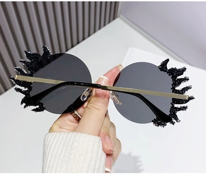Détail de lunettes de soleil rondes sans monture avec strass noirs et branches dorées