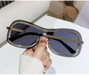 Dettaglio di occhiali da sole oversize senza montatura con bordo dorato e lenti grigio scuro