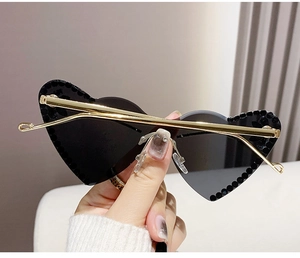 Close-up of heart-shaped rimless sunglasses with black rhinestones and gold metal temples