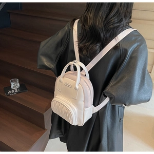 Detail view of cream mini backpack with ruched front pocket and metal logo plaque