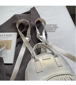 Detail of silver metallic backpack showing mesh texture and smooth wide shoulder strap