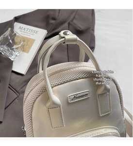 Detail of white leather and mesh bag with metal logo on a minimalist gray background