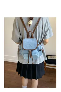 Detail of light blue denim backpack with brown leather trim and buckle on a model