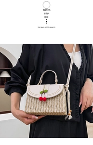 Detail of straw handbag featuring white leather flap, cherry charms and tassel rope strap