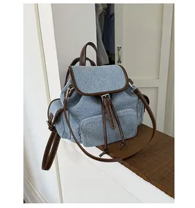 Detail of blue denim backpack with brown leather trim and zipper pocket on a wooden sill