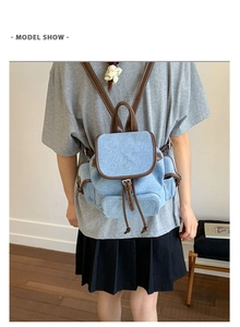 Blue denim backpack with brown leather trim shown on model back in a minimalist setting