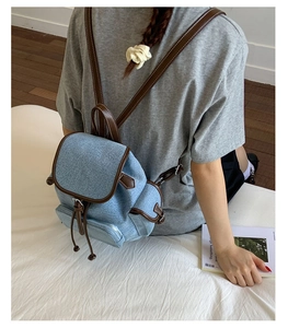 Light blue denim mini backpack with brown leather trim and drawstring closure on model