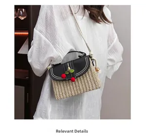 Detail of straw crossbody bag with cherry charms and thick rope strap on shoulder