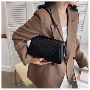 Detail of black crocodile pattern shoulder bag with V-shaped flap on model