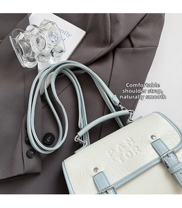 Detail of the PAN TOR embossed logo and metallic buckle on the contrast flap bag
