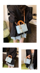 Detail of light blue textured square bag with brown handles and pearl bow charm