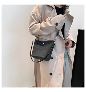 Détail du sac seau noir tissé avec clou cœur argenté sur un trench-coat beige