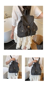 Detail view of a black denim backpack with drawstring closure and metal buckle pockets