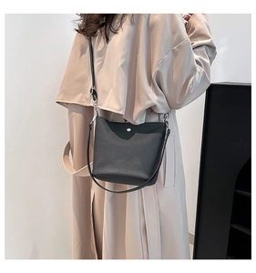 Détail d'un sac seau noir tressé avec garnitures argentées sur un trench beige