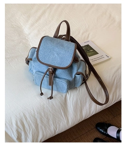 Detail of light blue denim mini backpack with brown leather trim and bronze metal buckles