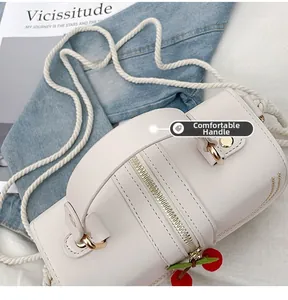 Detail of white cylindrical straw bag with cotton rope strap and cherry zipper charm