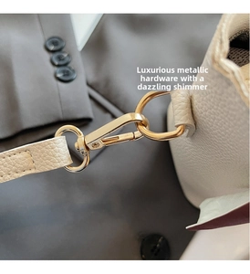 Macro view of bright gold lobster clasp hardware and pebble grain leather on beige bucket bag