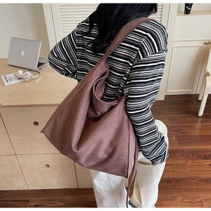 Borsa hobo in camoscio marrone con tracolla larga indossata da una persona in un ufficio a casa