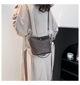 Gros plan d'un sac seau marron foncé porté sur un trench beige avec des boucles en argent