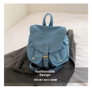 Detail of blue denim backpack with buckle strap and stitching on gray suit background
