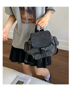 Detail of dark grey washed denim backpack with black leather trim and white stitching
