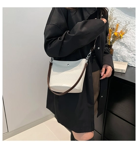 Détail du sac seau tissé crème avec bandoulière en cuir marron foncé et anneaux argentés