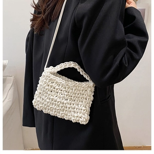 Detailed cross-weave texture of a white handmade knit crossbody bag on a black blazer