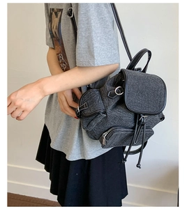 Detail of grey denim backpack with black leather trim and contrast stitching on model