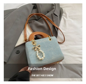 Close-up of denim crossbody bag with brown leather handles and pearl bow charm