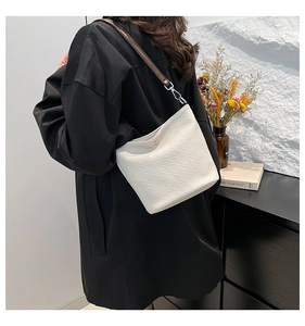 Sac seau blanc minimaliste avec bandoulière marron porté par un mannequin chic
