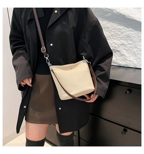 Gros plan du sac seau tissé beige avec bandoulière en cuir marron et détails argentés